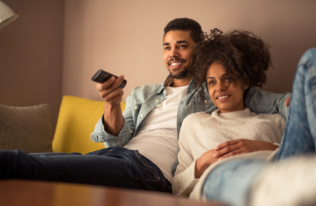 Man en vrouw liggend op de bank met TV-afstandsbediening in de hand. Ze kijken TV.