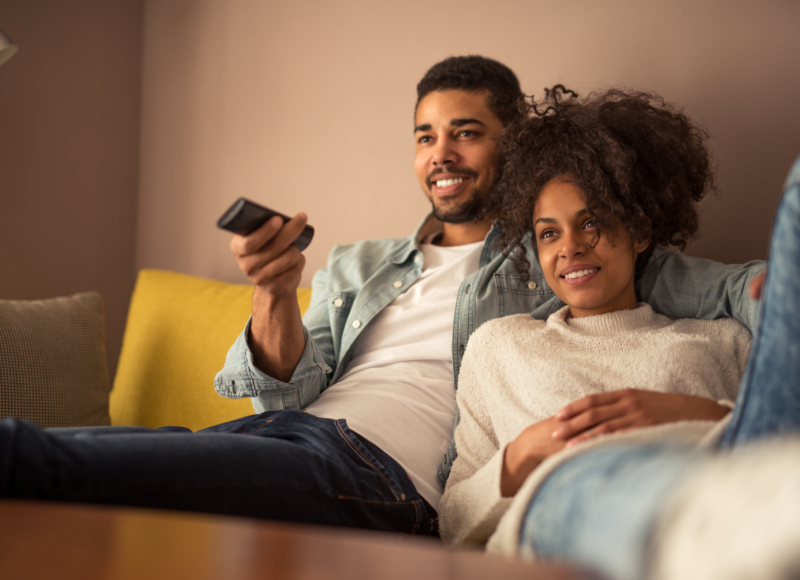 Man en vrouw liggend op de bank met TV-afstandsbediening in de hand. Ze kijken TV.