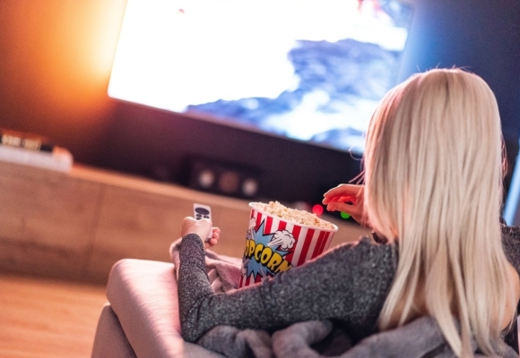 Vrouw kijkt tv met bak popcorn