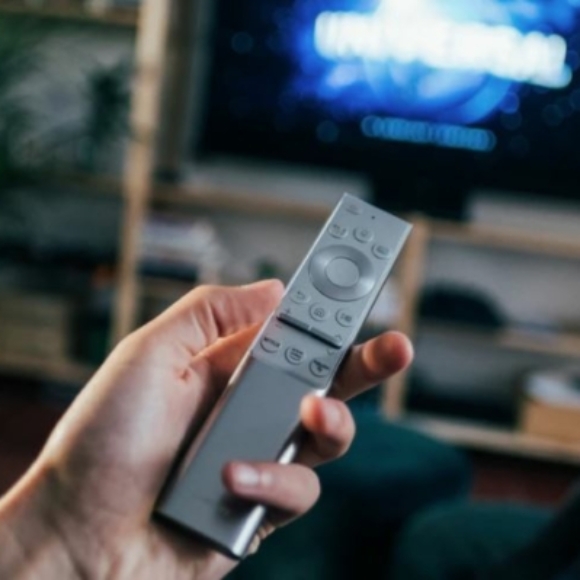 Hand met afstandsbediening gericht op een tv in een woonkamer