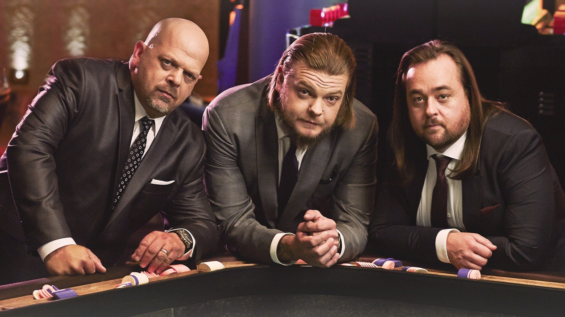 3 mannen in pak hangend op een tafel terwijl ze de camera inkijken